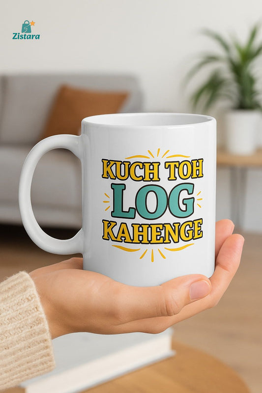 White ceramic mug with "KUCH TOH LOG KAHENGE" printed in colorfult text held in a hand, with a blurred indoor background