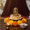 Gold statue on a white pedestal with marigold flowers and a lit candle on a dark surface.